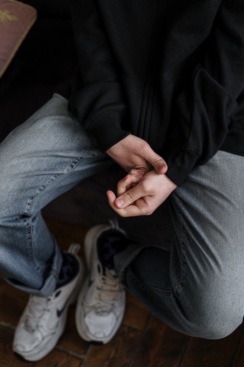 A young man in casual attire sitting with hands clasped, expressing contemplation.