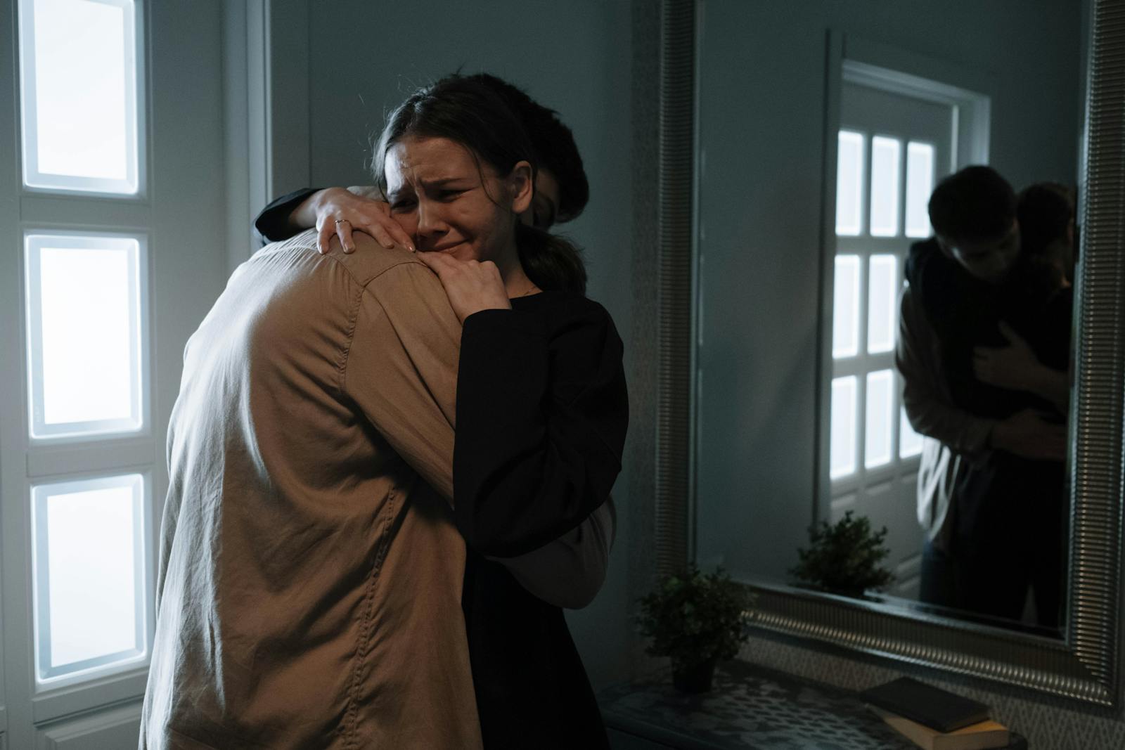 A touching scene of two adults hugging with reflection in mirror, indicating emotional support.