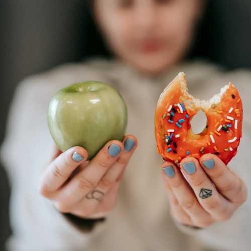 A close-up of a person holding an apple and a donut, symbolizing the choice between healthy eating and indulgence.